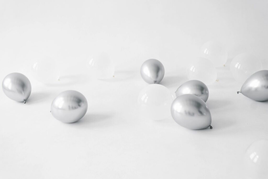 Festive Silver And White Balloons Scattered On Floor In White Studio