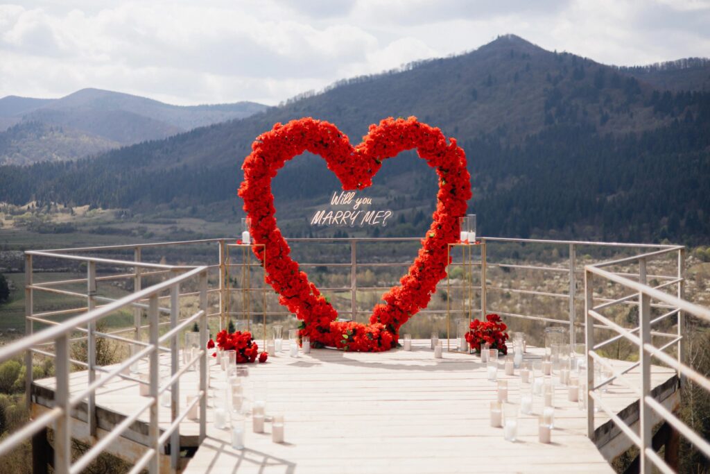 Romantic marriage proposal setup with a heart shaped floral arch and mountain view